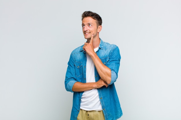 Hombre guapo joven sonriendo felizmente y soñando despierto o dudando, mirando hacia un lado