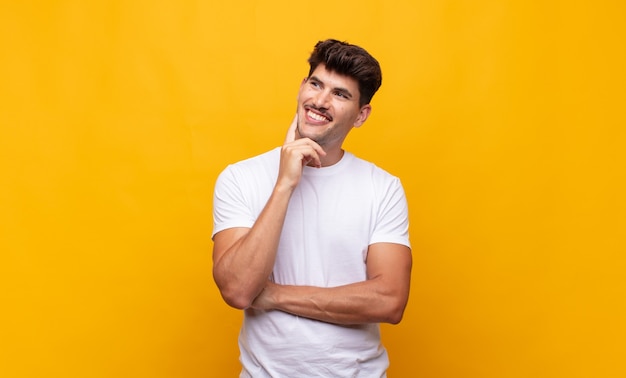 Hombre guapo joven sonriendo felizmente y soñando despierto o dudando, mirando hacia un lado