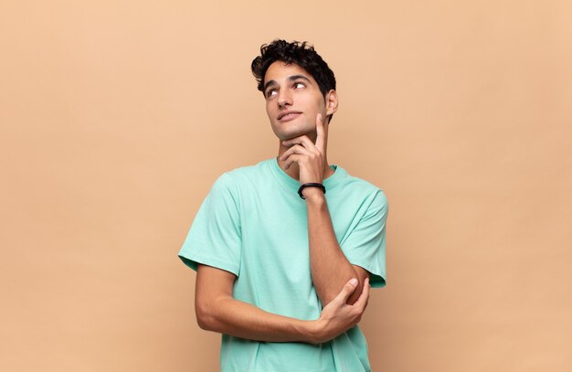 Hombre guapo joven sonriendo felizmente y soñando despierto o dudando, mirando hacia un lado