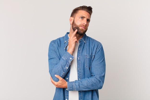 Foto hombre guapo joven sonriendo felizmente y soñando despierto o dudando