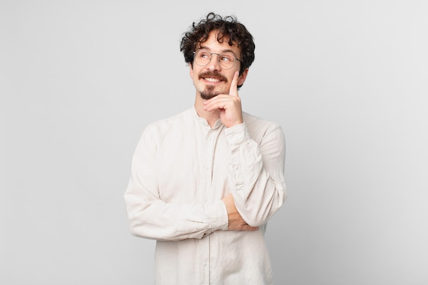 Hombre guapo joven sonriendo felizmente y soñando despierto o dudando