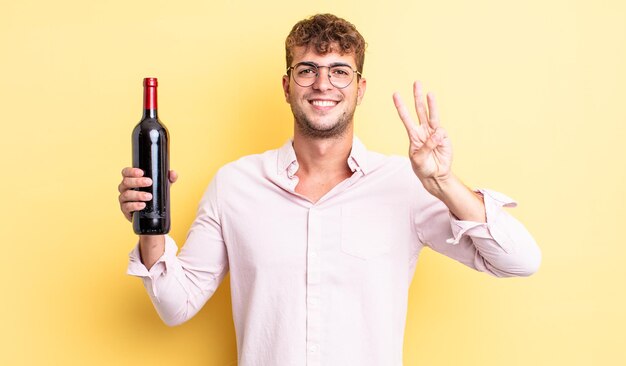 Hombre guapo joven sonriendo y luciendo amigable mostrando el concepto de botella de vino número tres