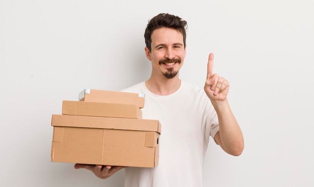 Hombre guapo joven sonriendo y luciendo amigable mostrando el concepto de cajas de envío número uno