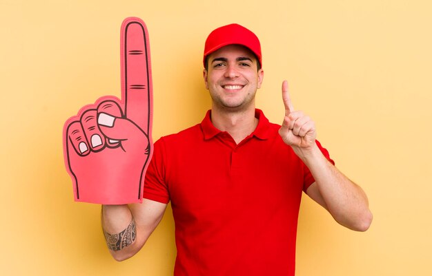 Hombre guapo joven sonriendo y luciendo amigable mostrando el concepto de mano número uno número uno