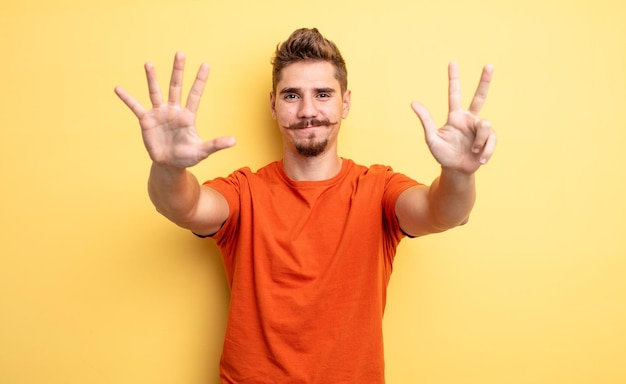 Hombre guapo joven sonriendo y luciendo amigable mostrando el número ocho u octavo con la mano hacia adelante contando el extraño concepto de bigote