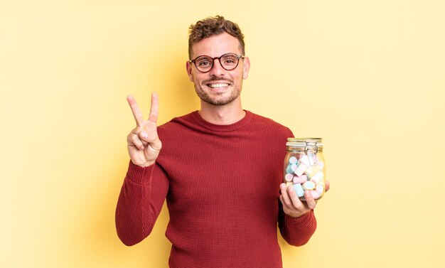 Hombre guapo joven sonriendo y luciendo amistoso mostrando el concepto de caramelos de gelatina número dos