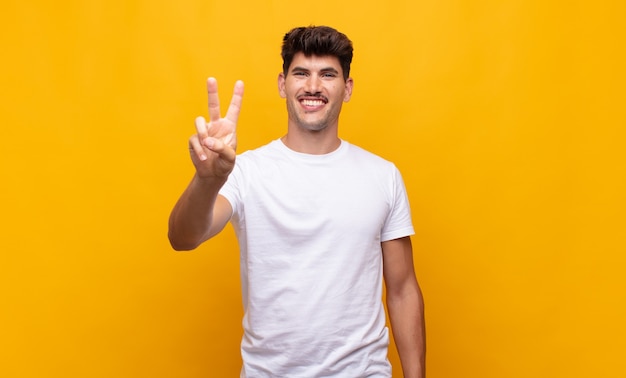 Hombre guapo joven sonriendo y mirando amigable, mostrando el número dos o el segundo con la mano hacia adelante, contando hacia atrás