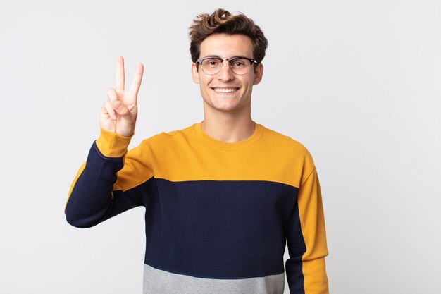 Hombre guapo joven sonriendo y mirando amigable, mostrando el número dos o el segundo con la mano hacia adelante, contando hacia atrás