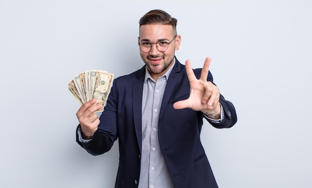 Hombre guapo joven sonriendo y mirando amigable, mostrando el número tres. concepto de billetes de dólar