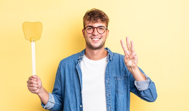 Hombre guapo joven sonriendo y mirando amigable, mostrando el número tres. concepto matamoscas