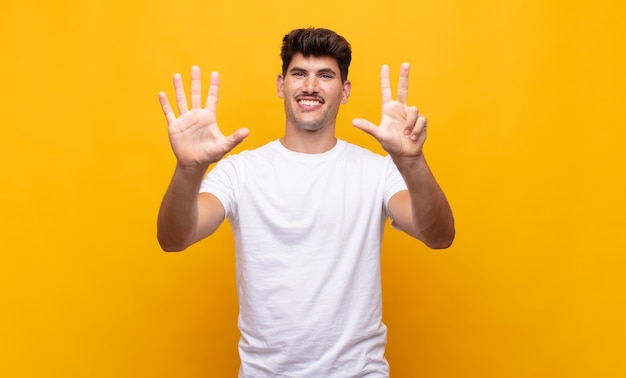 Hombre guapo joven sonriendo y mirando amigablemente, mostrando el número ocho u octavo con la mano hacia adelante, contando hacia atrás