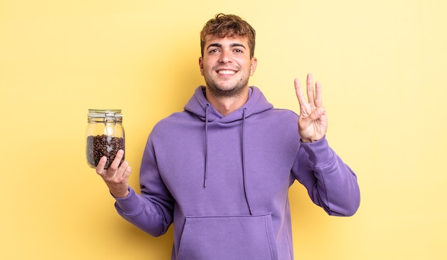 Hombre guapo joven sonriendo y mirando amistoso, mostrando el número tres. concepto de granos de cafe