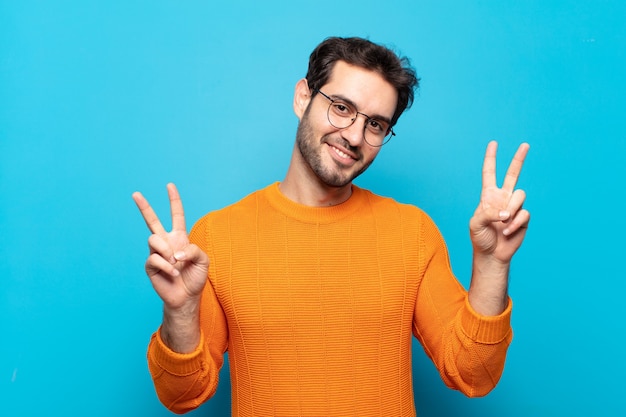 Hombre guapo joven sonriendo y mirando feliz, amigable y satisfecho, gesticulando victoria o paz con ambas manos