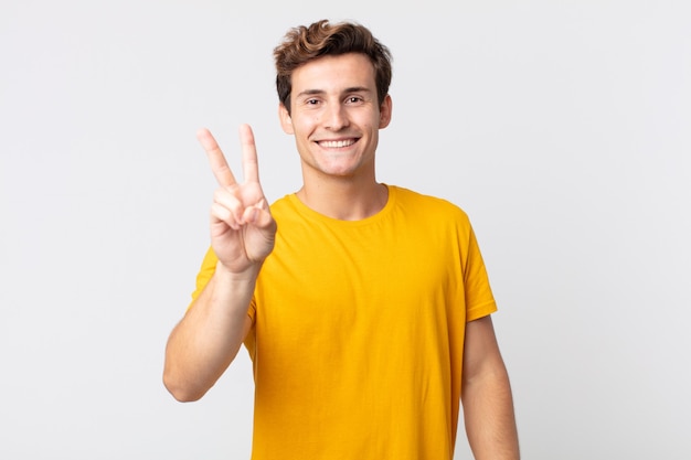 Hombre guapo joven sonriendo y mirando feliz, despreocupado y positivo, gesticulando victoria o paz con una mano