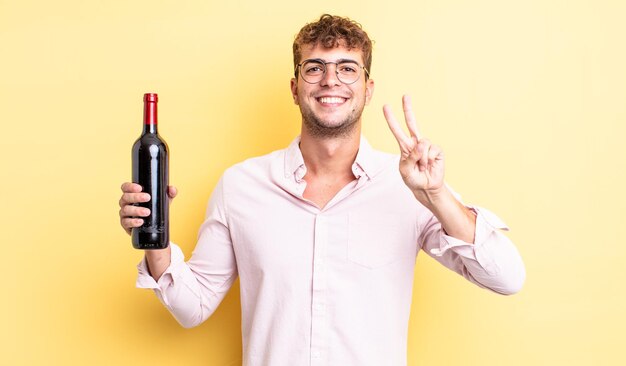 Hombre guapo joven sonriendo y mirando feliz, gesticulando victoria o paz. concepto de botella de vino