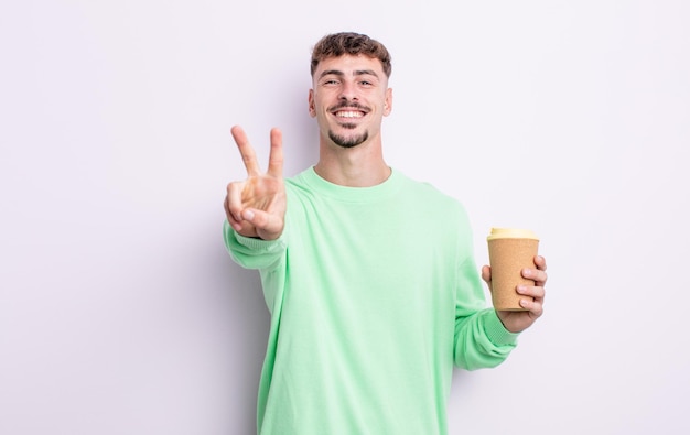 Hombre guapo joven sonriendo y mirando feliz, gesticulando victoria o paz. concepto de café para llevar