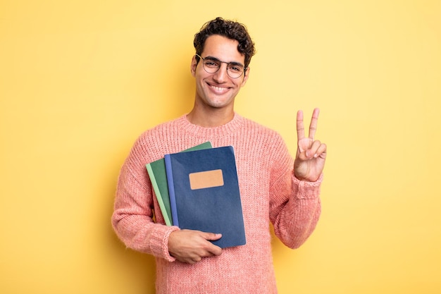 Hombre guapo joven sonriendo y mirando feliz, gesticulando victoria o paz. concepto de cuaderno