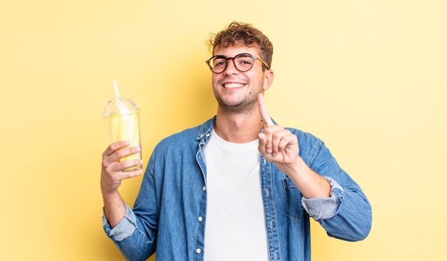 Hombre guapo joven sonriendo con orgullo y confianza haciendo el número uno. concepto de batido