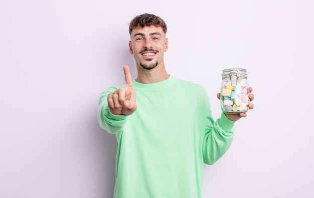 Hombre guapo joven sonriendo con orgullo y confianza haciendo el número uno. concepto de caramelos de gelatina