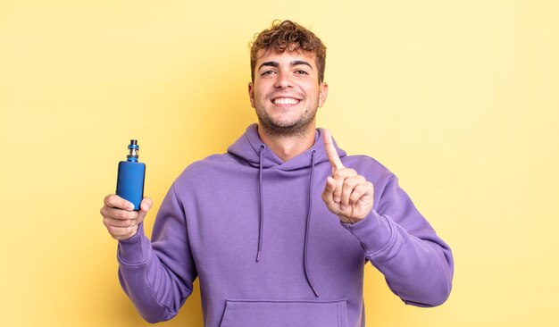 Hombre guapo joven sonriendo con orgullo y confianza haciendo el número uno. concepto de vaporizador