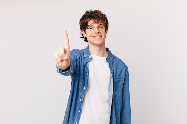 Hombre guapo joven sonriendo con orgullo y confianza haciendo el número uno