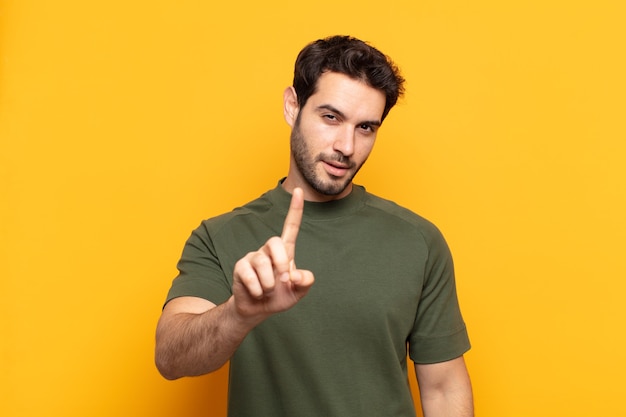 Hombre guapo joven sonriendo con orgullo y confianza haciendo pose número uno triunfalmente