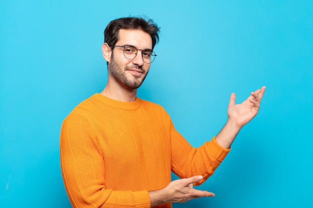 Hombre guapo joven sonriendo con orgullo y confianza, sintiéndose feliz y satisfecho y mostrando un concepto en el espacio de la copia