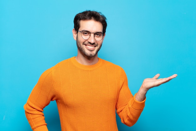 Hombre guapo joven sonriendo, sintiéndose confiado, exitoso y feliz, mostrando concepto o idea en el espacio de la copia en el lateral