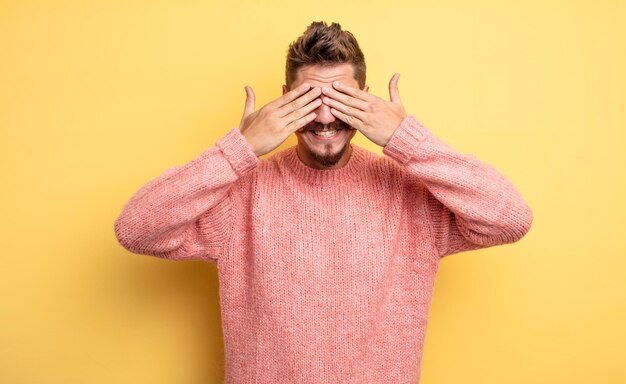Hombre guapo joven sonriendo y sintiéndose feliz, cubriendo los ojos con ambas manos y esperando una sorpresa increíble. extraño concepto de bigote