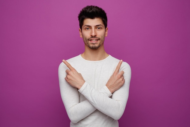 Hombre guapo joven sonriente mirando a la cámara apuntando hacia arriba sobre fondo púrpura