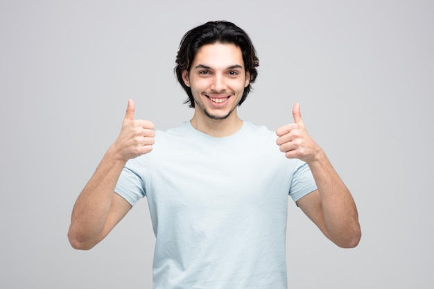 Hombre guapo joven sonriente mirando a la cámara mostrando los pulgares hacia arriba aislado sobre fondo blanco.