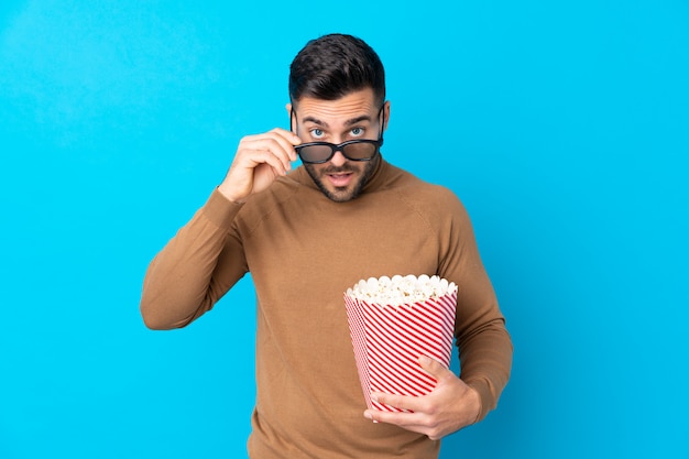 Hombre guapo joven sorprendido con gafas 3d y sosteniendo un gran cubo de palomitas de maíz