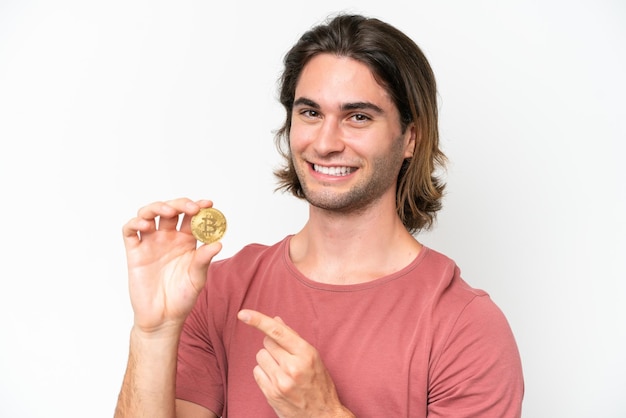 Hombre guapo joven sosteniendo un Bitcoin aislado sobre fondo blanco y apuntándolo