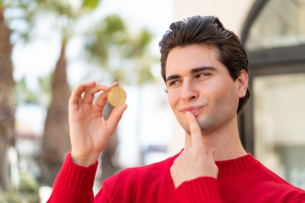 Hombre guapo joven sosteniendo un Bitcoin y pensando