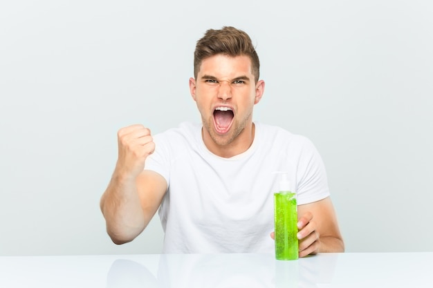 Hombre guapo joven sosteniendo una botella de aloe vera animando despreocupado y emocionado. Concepto de victoria.