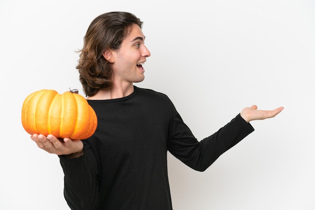 Hombre guapo joven sosteniendo una calabaza aislada sobre fondo blanco con expresión de sorpresa mientras mira de lado