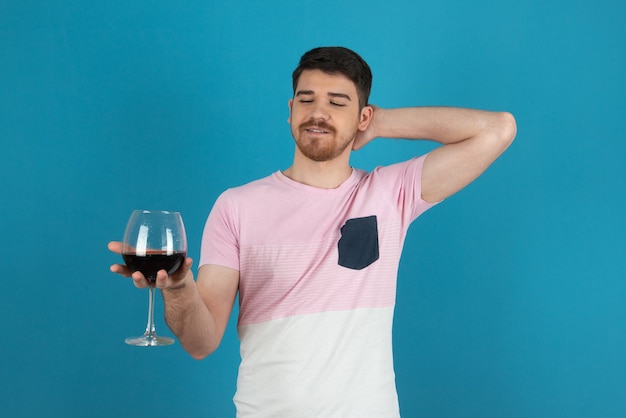 Hombre guapo joven sosteniendo una copa de vino en un azul.