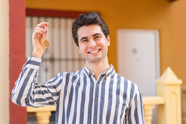 Hombre guapo joven sosteniendo llaves de casa con expresión feliz