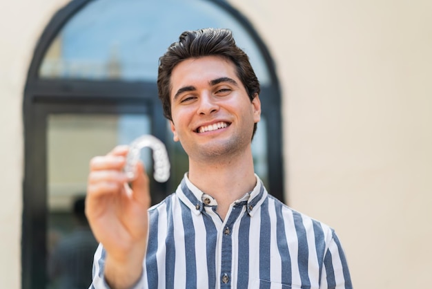 Hombre guapo joven sosteniendo llaves invisibles al aire libre con expresión feliz