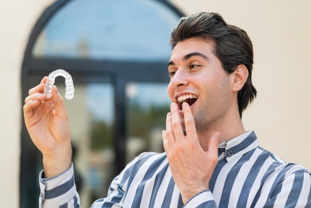 Hombre guapo joven sosteniendo llaves invisibles al aire libre con sorpresa y expresión facial conmocionada