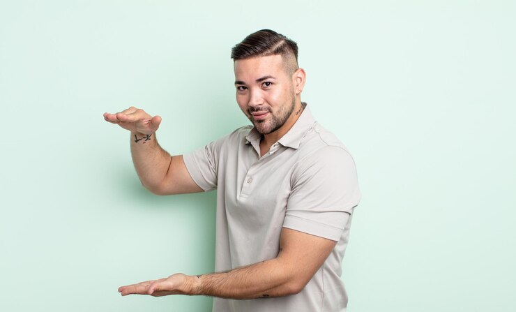 Foto hombre guapo joven sosteniendo un objeto con ambas manos en el espacio de copia lateral, mostrando, ofreciendo o publicitando un objeto