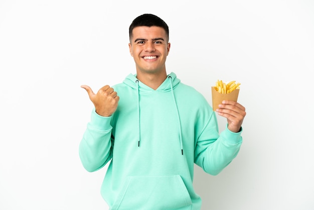 Foto hombre guapo joven sosteniendo patatas fritas sobre fondo blanco aislado apuntando hacia el lado para presentar un producto