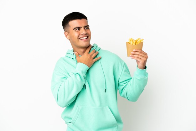 Hombre guapo joven sosteniendo patatas fritas sobre fondo blanco aislado mirando hacia arriba mientras sonríe