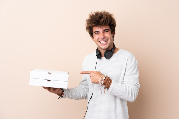 Hombre guapo joven sosteniendo una pizza sobre pared aislada y apuntando