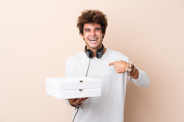 Hombre guapo joven sosteniendo una pizza sobre pared aislada con expresión facial sorpresa