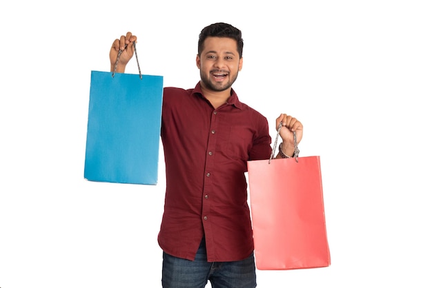 Hombre guapo joven sosteniendo y posando con bolsas de compras sobre un fondo blanco.