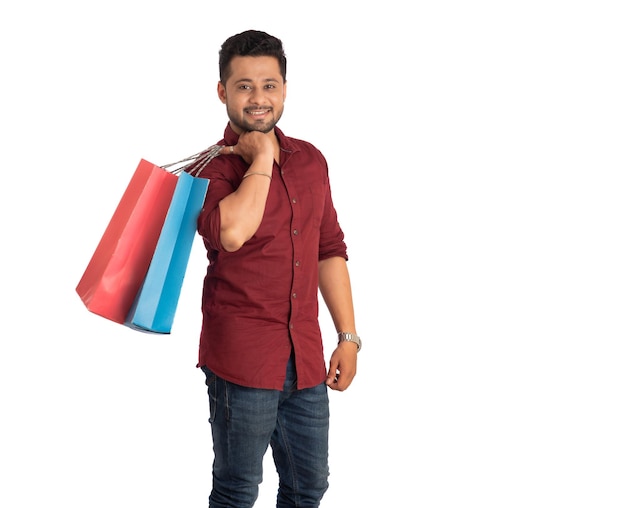 Hombre guapo joven sosteniendo y posando con bolsas de compras sobre un fondo blanco.