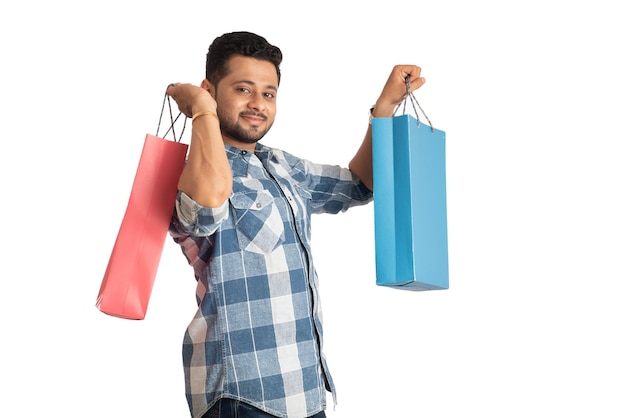 Hombre guapo joven sosteniendo y posando con bolsas de compras sobre un fondo blanco.