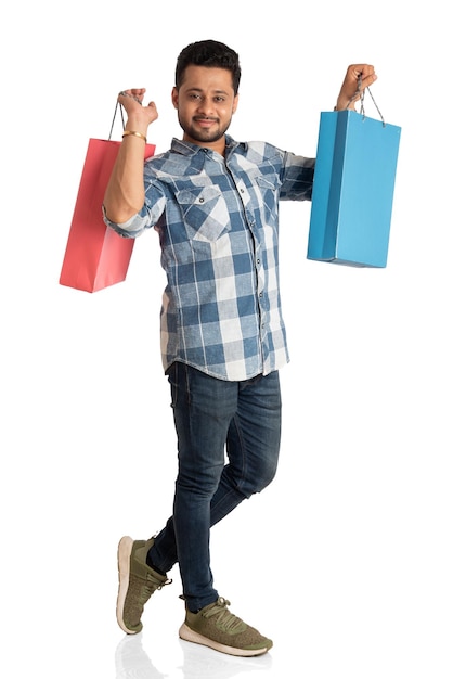 Hombre guapo joven sosteniendo y posando con bolsas de compras sobre un fondo blanco.