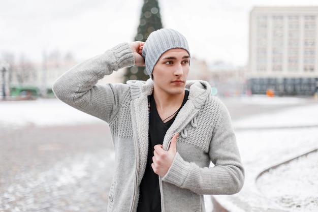 Hombre guapo joven en un suéter de invierno vintage y gorro de punto posando en un día de nieve
